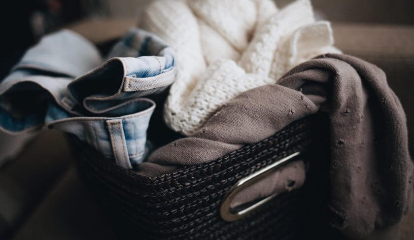 A basket filled with cluttered clothing items is pictured. It includes a pair of jeans, sweater and shirt.