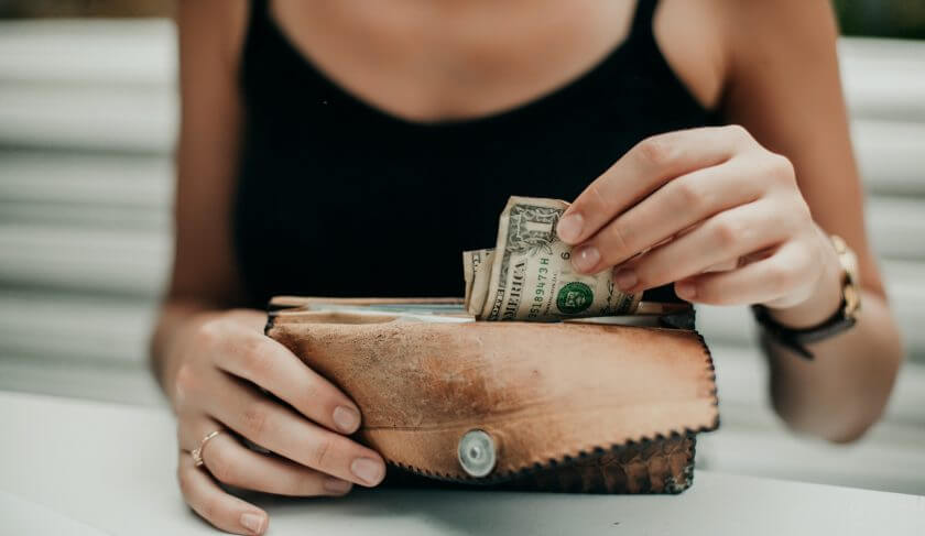 A woman in a black tank top pulls dollar bills out of a leather wallet