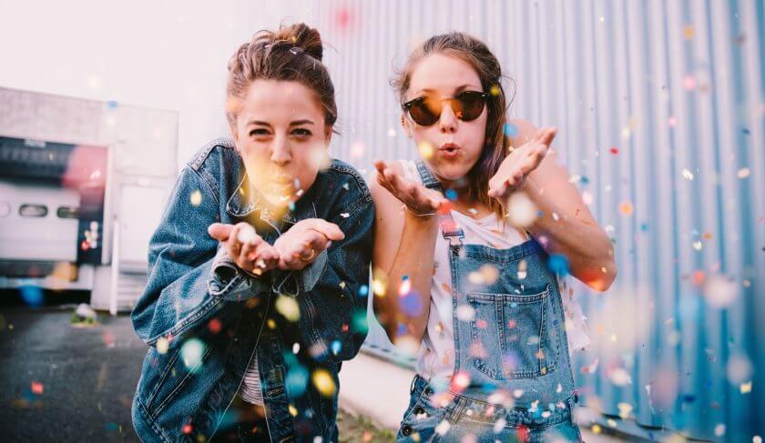 Two friends dressed in blue blow glitter and confetti at the camera. This article explores how to make saving money fun.