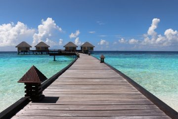 A wooden pier leads out over crystal clear blue ocean waters in the Caribbean.