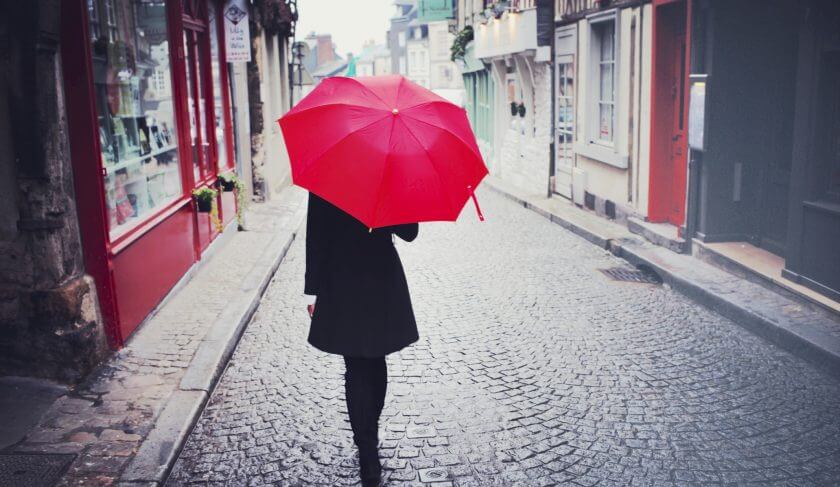 A woman walks down a cobblestone street holding a red umbrella