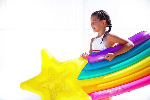 a little girl smiles in a rainbow float with an inflatable star as she gets ready to jump into the swimming pool.