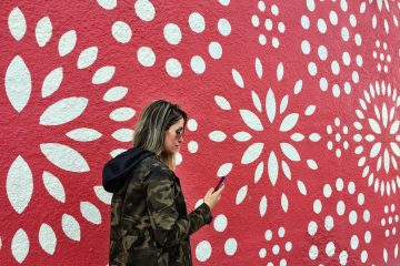 A woman stands in front of a red and white mural looking at her phone.