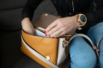 This photo depicts a close up of a woman's hands looking through a tan and white bag.