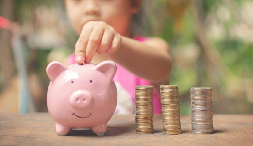 A young girl dressed in pink puts quarters into a pink piggy bank.