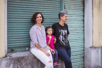 Two moms lean against a garage door with their daughter between them.