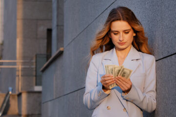 A woman stands outdoors looking at her money and counting it.