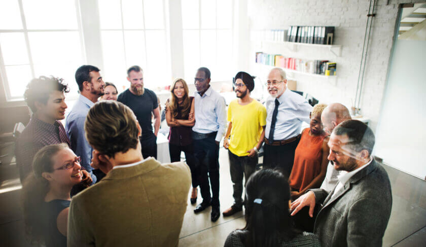 Group of colleagues in an office standing in a circle and talking and laughing together.