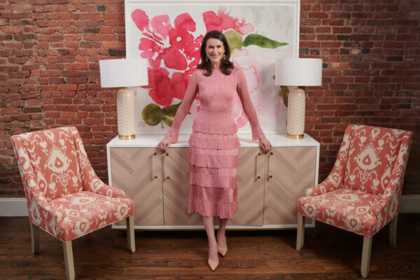 Auctuioneer Lydia Fenet stands near a sofa wearing a pink dress, discussing How To Be More Confident