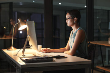 A woman works at her computer at night, studying a diversified stock portfolio