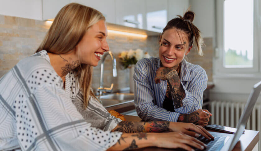 A lesbian couple works together at a computer to discuss the topic of love and money, and prevent money fights