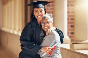 A college graduate wearing a cap and gown gets a hug from her mother