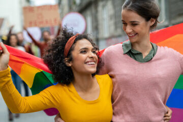 An image of two happy women at a pride parade, with rainbow flags