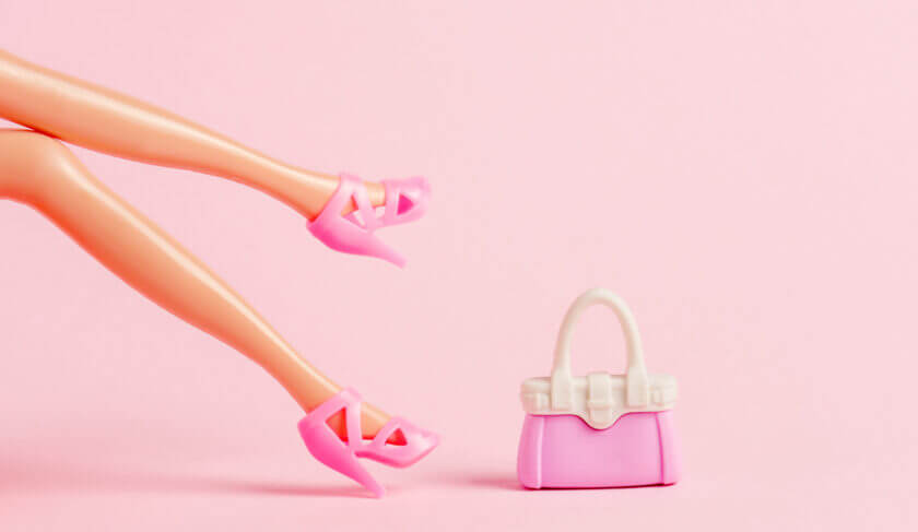 A barbie doll with high heels and little pink purse on pastel pink background. This article discusses whether Barbie Stock (Mattel) is a good investment.