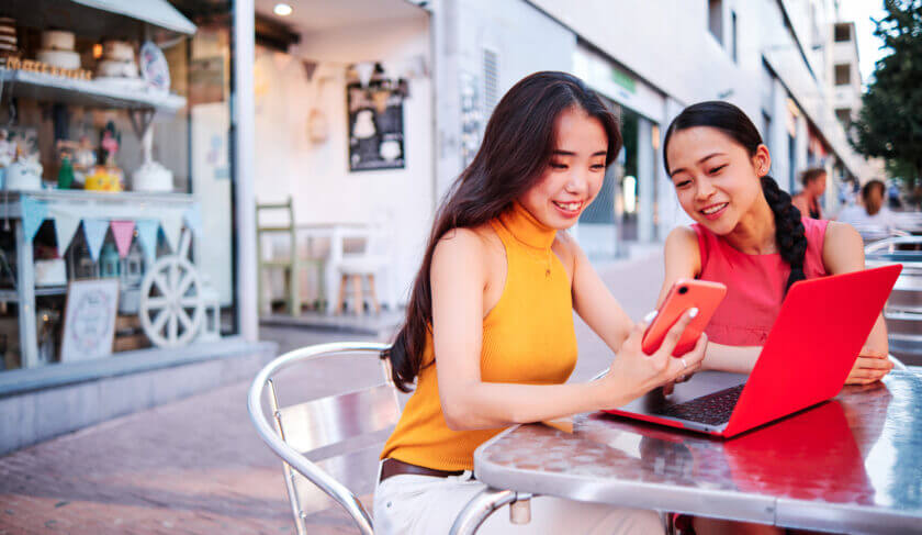 two women sit outdoors at a sidewalk cafe and look at a laptop together. We discuss first time investing and how women can get started