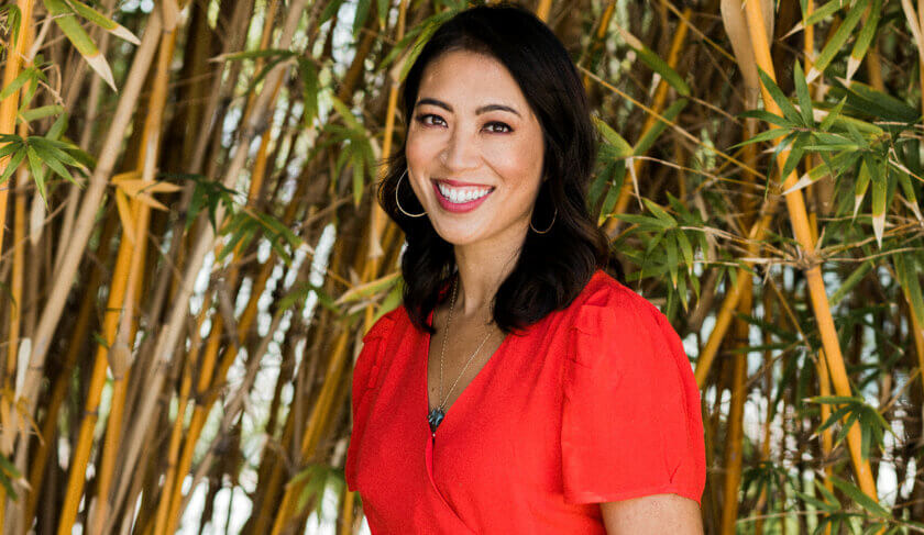 NPR reporter Elise Hu standing in a bamboo forest wearing red