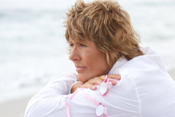 Diana Nyad wearing pink, holding pink goggles, and looking at the ocean