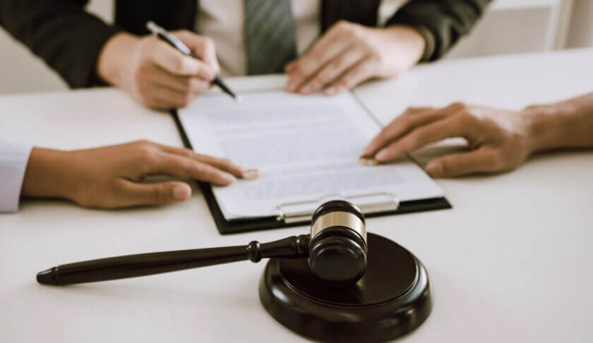 A couple sits at a table with a divorce attorney and signs paperwork.