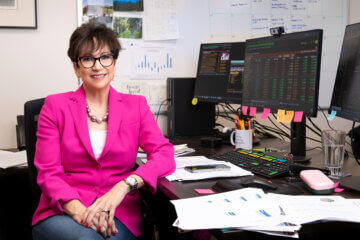 Nancy Tengler wears a pink suit jacket and sits at her desk at the office.