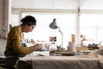 a woman sits in her workshop and creates pottery