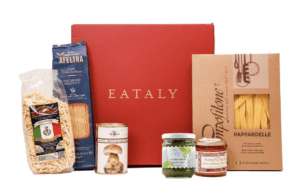 A terracotta colored box is pictured at center. On either side are components of pasta dinners, including three bags of pasta. 