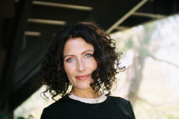 Lisa Edelstein wearing black in profile outside smiling at the camera.