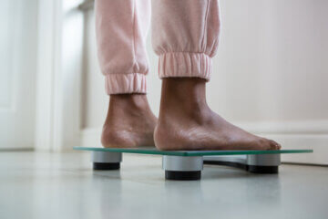 A woman in pink sweatpants stands on a scale. All you can see is the bottom of her pants, along with her feet.