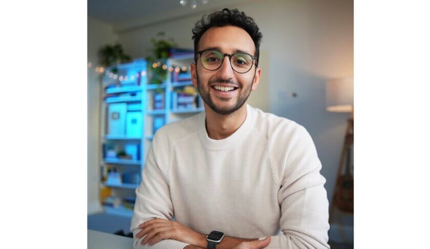 Ali Abdaal wears glasses and smiles at the camera with his arms crossed.
