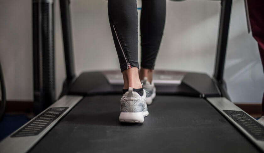 This photo shows a close up of a woman on a treadmill. Only her lower legs and feet are shown.