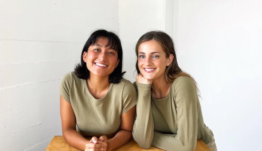 Oddli cofounders Jensen Neff and Ellie Chen wear sea green shirts and smile in front of a white background.