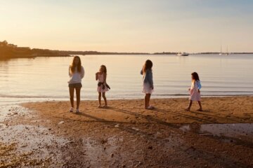 Four young women stand alongside the seashore at sunset