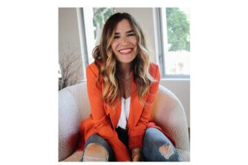 Headshot of Alli Webb wearing an orange blazer and smiling at the camera.